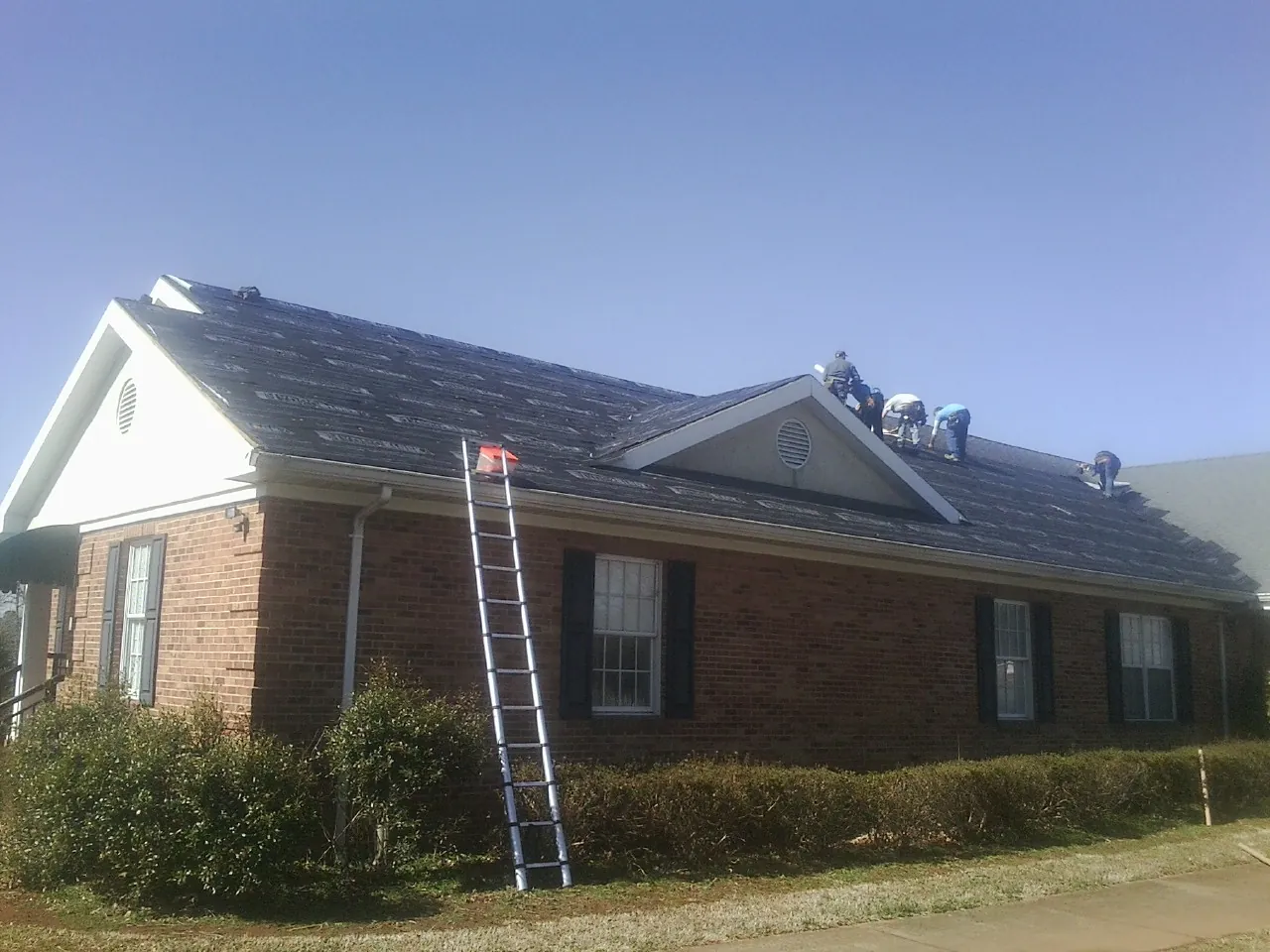 Crew tearing shingles off a brick ranch roof with a ladder set — Metal Roof Repair work by our crew in Curtis