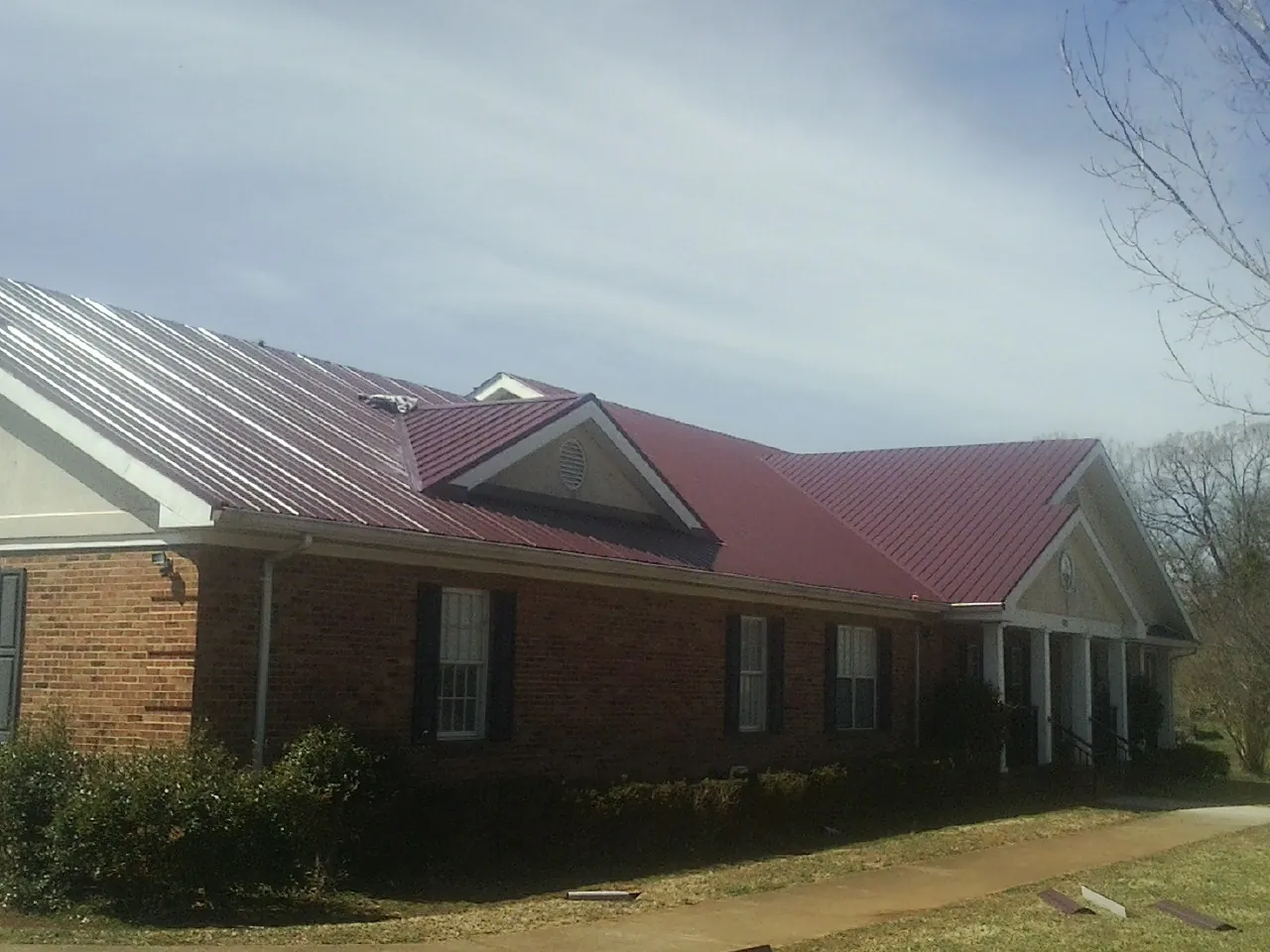 Red metal roof with gabled entries on a long brick building, from a Hail Damage Roof Repair job in Curtis