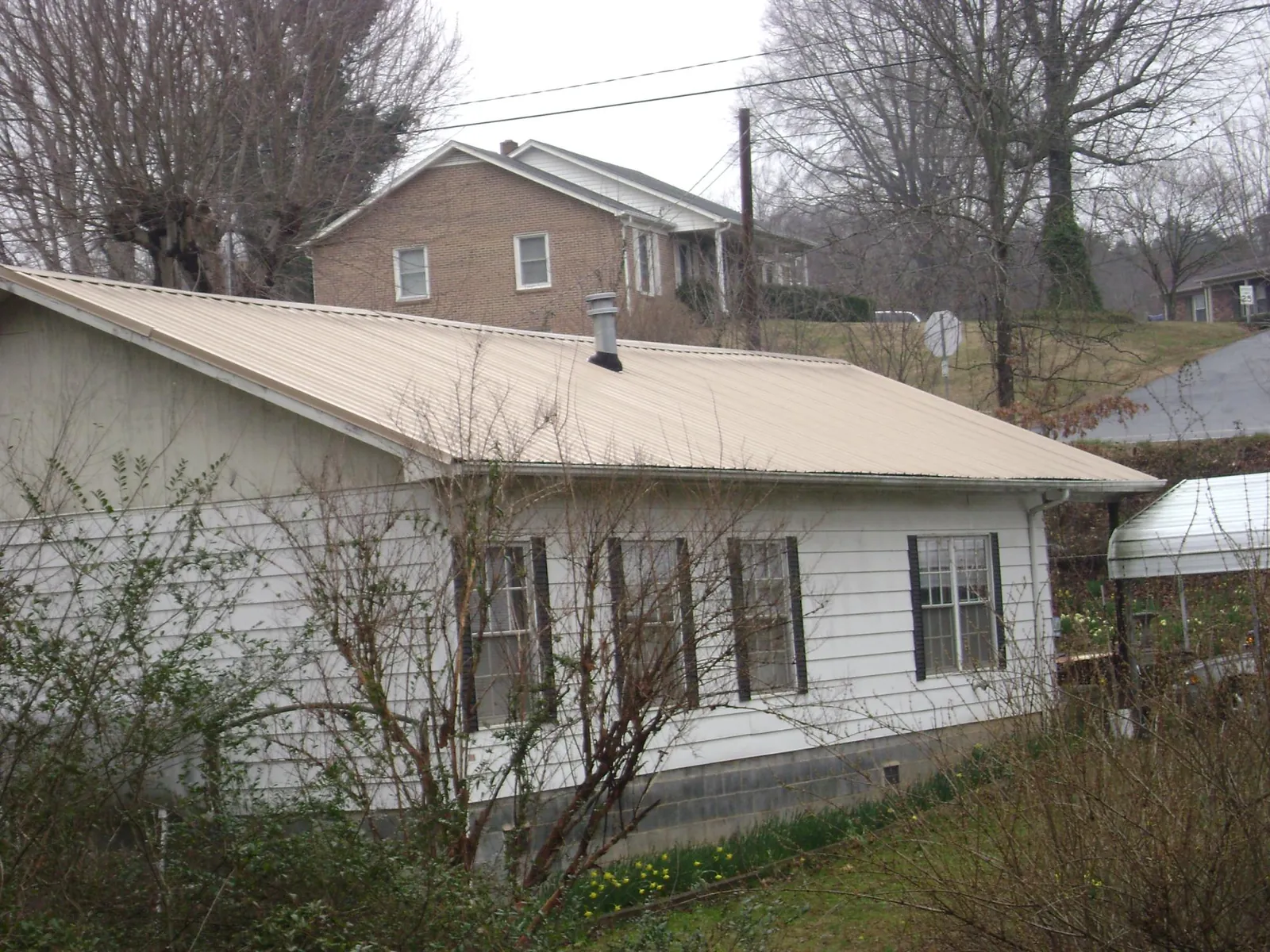 Tan metal roof on a white sided house set into a hillside — Commercial Roofing by Roofing Brothers in Curtis