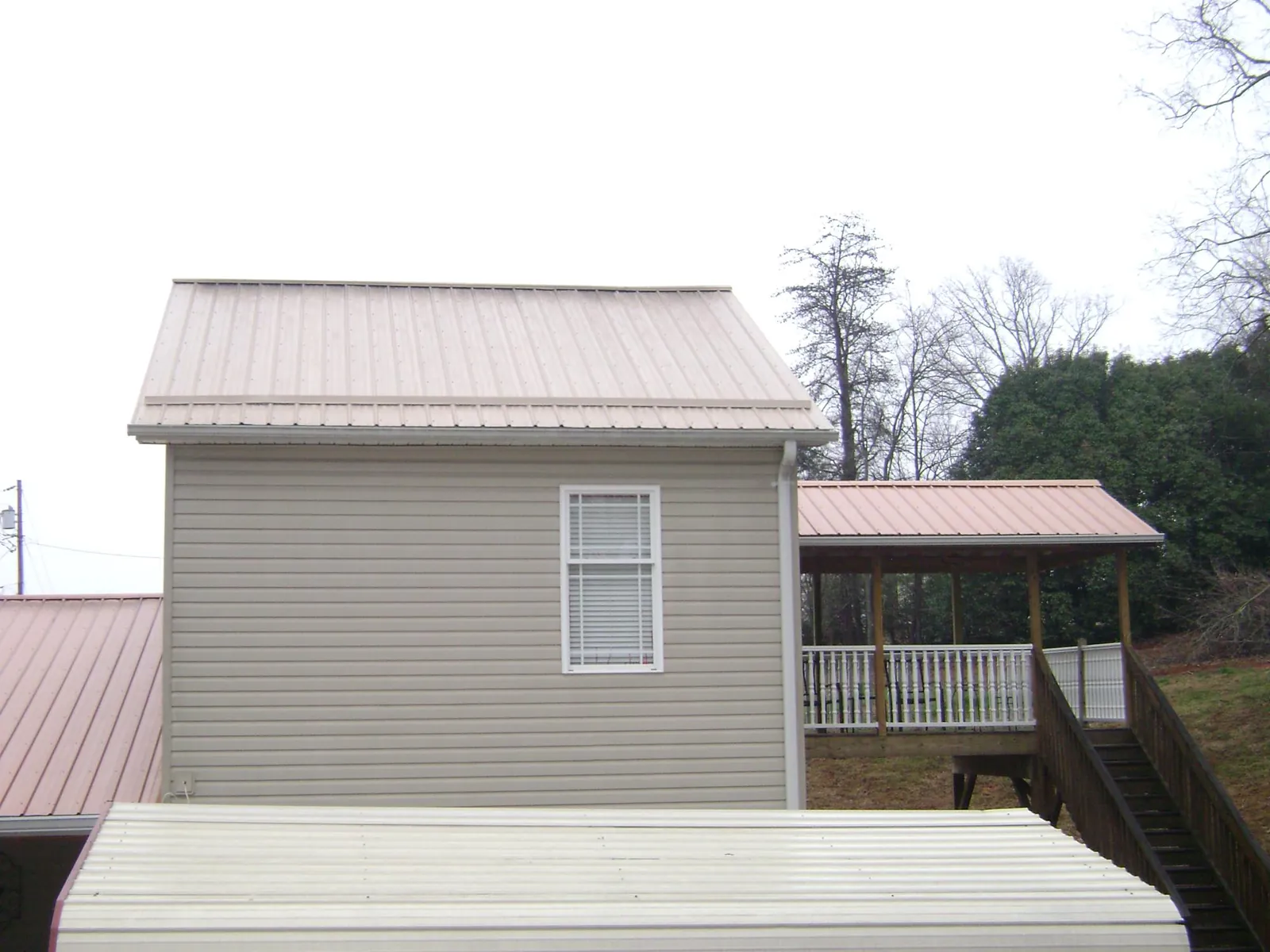 Tan metal roofs on a two story addition and attached porch, from a Roof Replacement job in Curtis