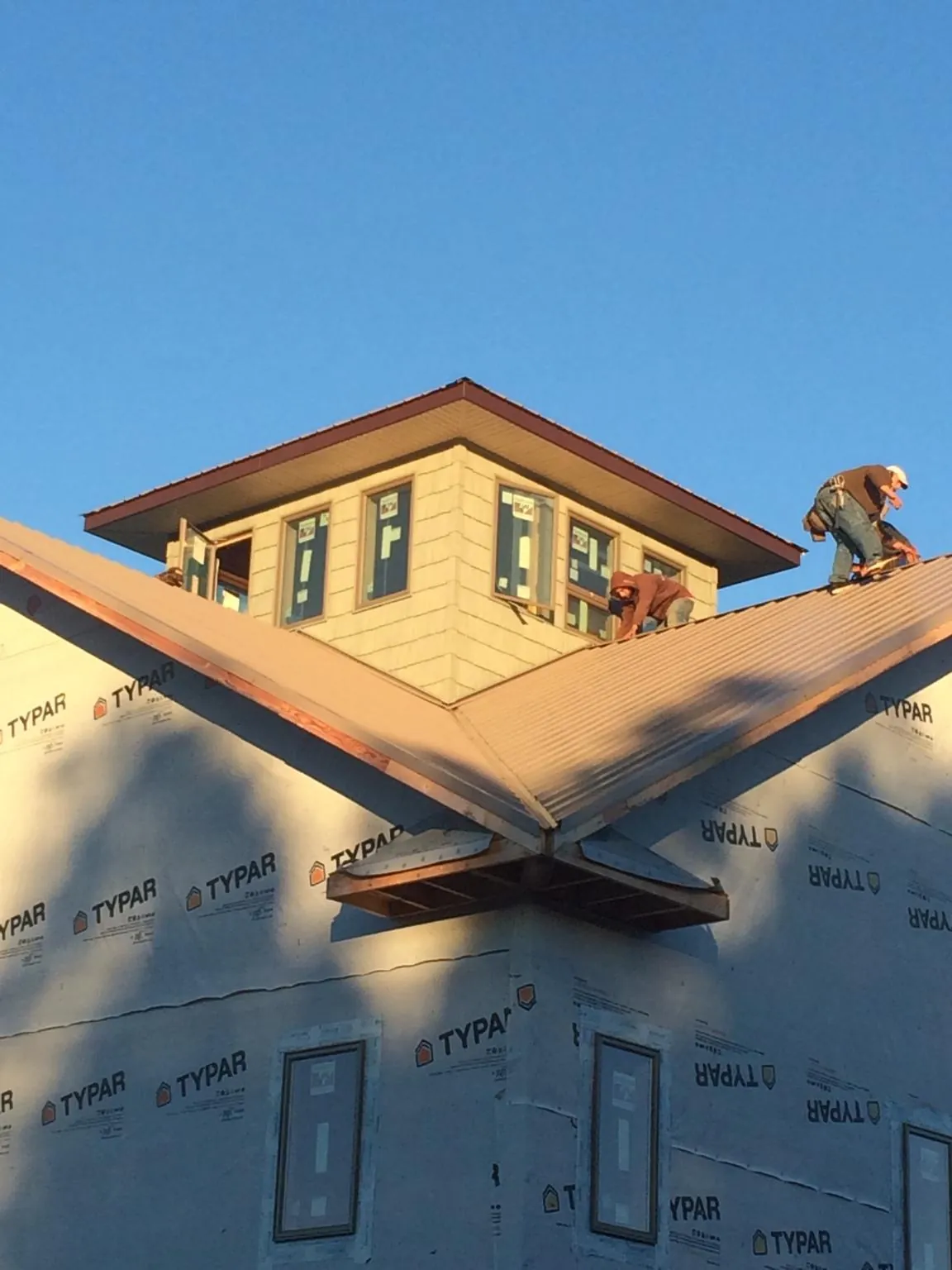 Roofers working around a rooftop cupola on a new metal roof at sunset — Roof Waterproofing in Curtis by Roofing Brothers